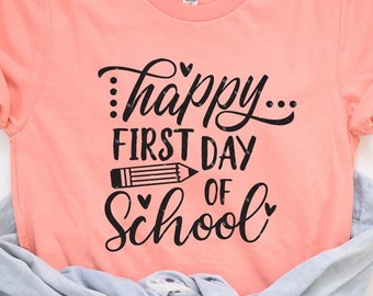 May include: A peach colored t-shirt with the text "...happy... first day of school" in black lettering. A black pencil is drawn between the words "first day" and "of school".