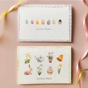Peut inclure: Deux cartes de vœux de Pâques avec des illustrations à l'aquarelle. La carte du haut présente des œufs colorés, et celle du bas un lapin, des fleurs et un arrosoir. Les deux cartes portent l'inscription "Joyeuses Pâques!"