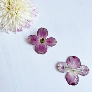 May include: Two purple flower hair clips with a white background. The flower clips are made from real pressed flowers.