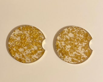May include: Two round white coasters with gold glitter embedded in the resin. The coasters have a cut-out for a cup.
