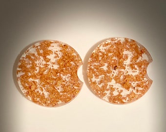 May include: Two round white coasters with a gold fleck design. The coasters have a cut-out for a cup.