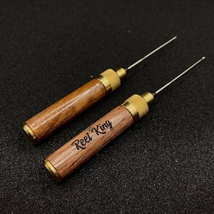 May include: Two wooden tools with brass accents and a needle-like tip. The tools are engraved with the words "Reel King".