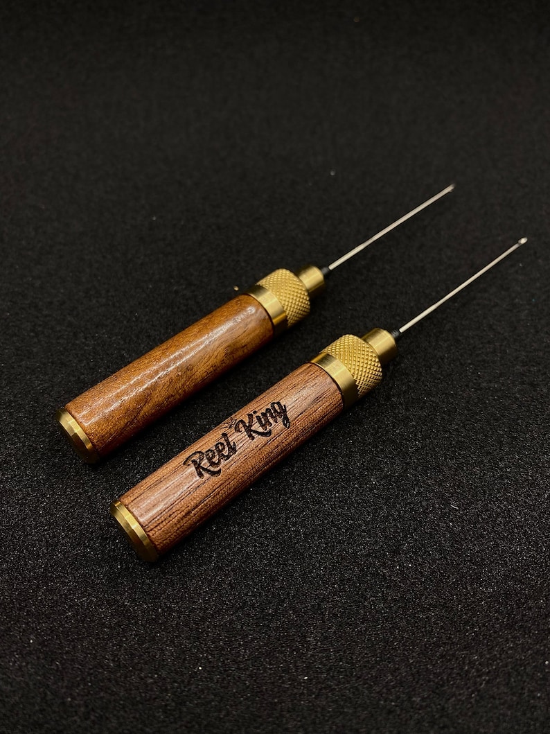 May include: Two wooden tools with brass accents and a needle-like tip. The tools are engraved with the words "Reel King".