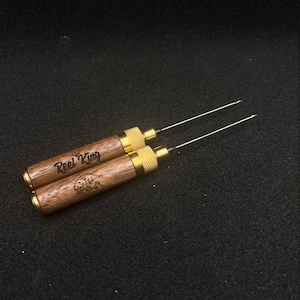 May include: Two wooden tools with gold metal tips and a brown wood handle. The handle is engraved with the words "Reel King" and a fish graphic.