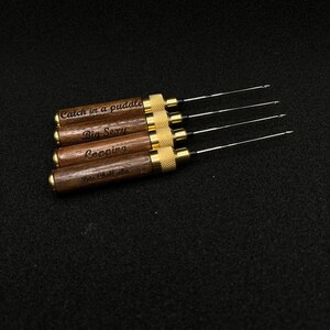 May include: Five wooden tools with gold metal accents and engraved text. The text reads "Catch in a puddle", "Big Sexy", "Copping", and "Pete Chocolata".