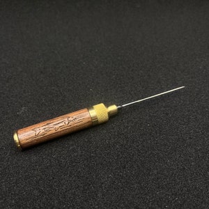 May include: A wooden and brass tool with a long, thin needle. The wooden handle is engraved with a fish design and the text "Fishin' Time".