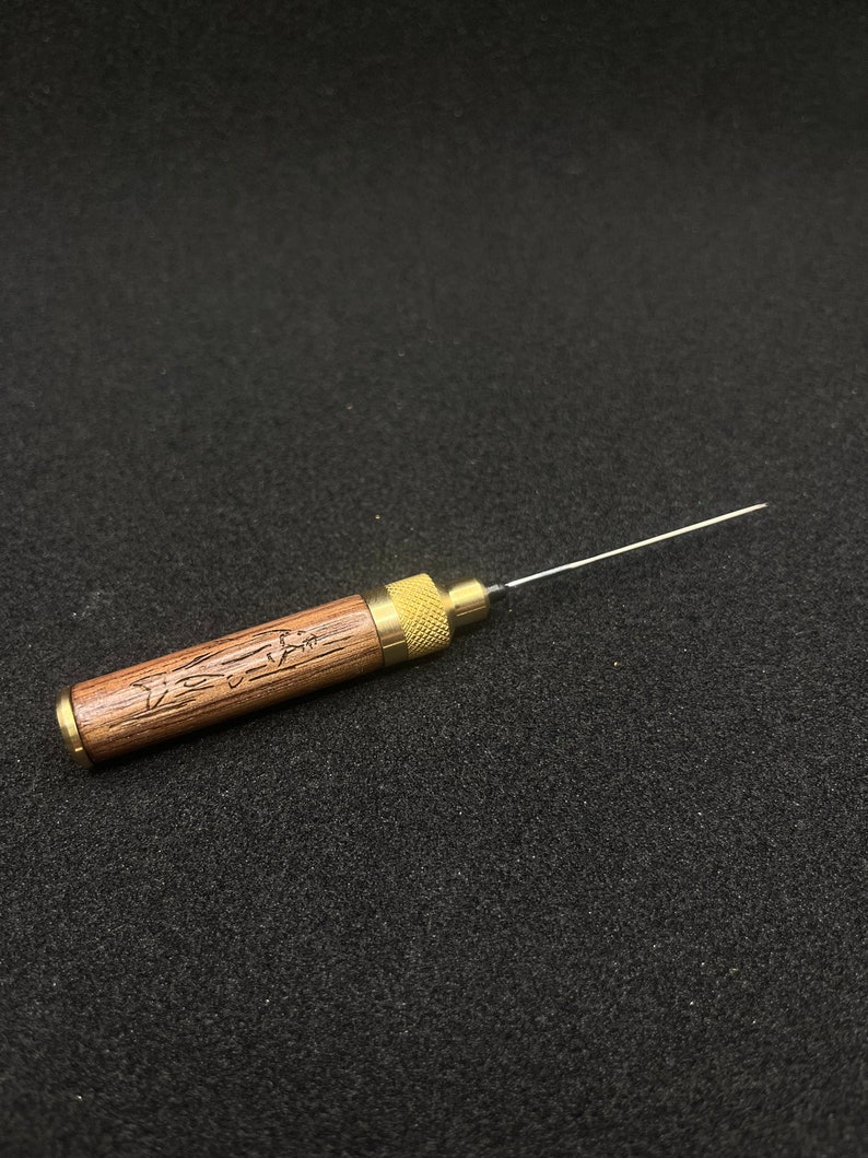 May include: A wooden and brass tool with a long, thin needle. The wooden handle is engraved with a fish design and the text "Fishin' Time".