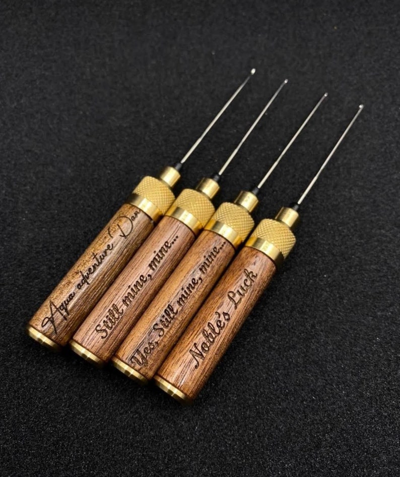 May include: Five wooden tools with brass accents and engraved text. The tools have a thin metal needle extending from the end. The text on the tools reads "Aqua adventure Dan", "Still mine, mine...", "Yes, Still mine, mine...", and "Noble's Luck".