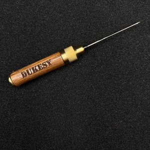 May include: A wooden tool with a brass tip and a metal knob. The tool is engraved with the word "DUKESY".