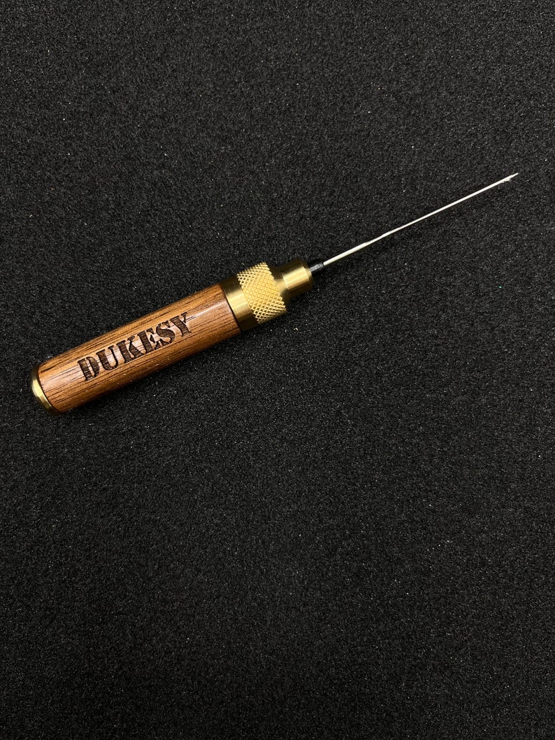 May include: A wooden tool with a brass tip and a metal knob. The tool is engraved with the word "DUKESY".