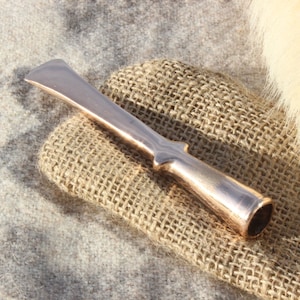 May include: A copper-coloured tool with a long, flat blade and a rounded handle. The tool is lying on a piece of hessian fabric.