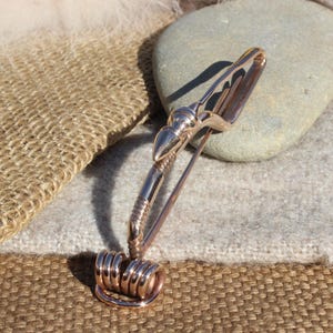 May include: A rose gold metal brooch with a curved design and a decorative spiral at the bottom.