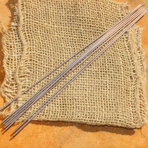 May include: A bundle of thin, silver-colored metal rods arranged on a piece of brown burlap fabric.