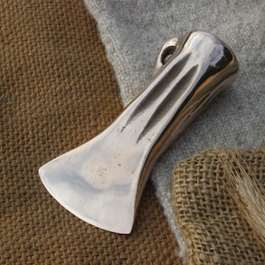 May include: A silver-coloured metal axe head with a smooth, rounded surface and a slightly curved blade. The axe head has a decorative groove pattern on the handle.