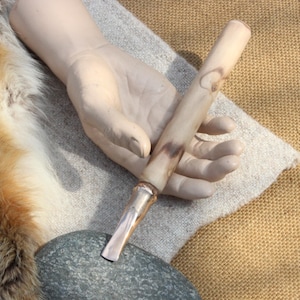 May include: A close-up of a wooden tool with a light brown and dark brown wood grain pattern. The tool has a rounded handle and a pointed tip.