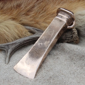 May include: A metallic, wedge-shaped tool with a polished, copper-toned finish. The object features a wide, flat blade edge that tapers towards a thicker, rounded handle end. The surface shows subtle variations in texture and colour, reflecting light.