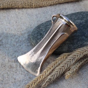 May include: A bronze axe head with a loop handle. The axe head is smooth and polished, with a sharp edge. The axe head is resting on a piece of hessian fabric.