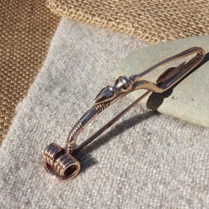 May include: A bronze Viking-style brooch with a decorative spiral design at the bottom and a stylized animal head at the top.