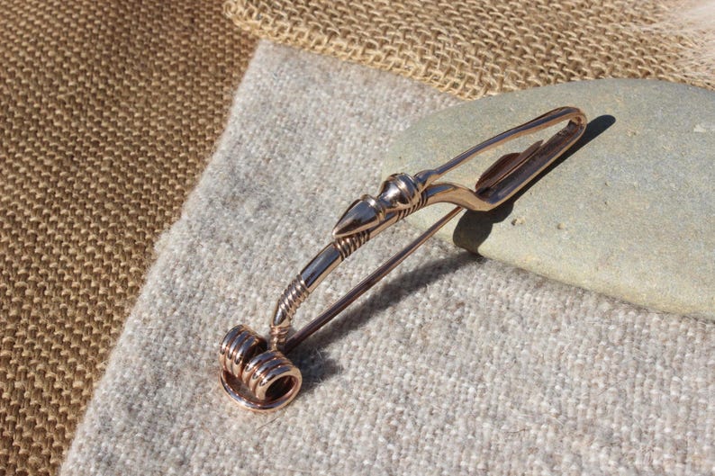 May include: A bronze Viking-style brooch with a decorative spiral design at the bottom and a stylized animal head at the top.