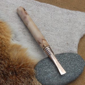 May include: A wooden tool with a brown and white wood grain pattern and a metal tip. The tool is lying on a grey stone and a brown fur surface.