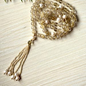 以下が含まれることがあります： 金色のシトリンビーズと白い真珠のアクセント、タッセルが付いた長いネックレス。ビーズはファセットカットされており、半透明な外観をしています。