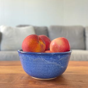 May include: A blue ceramic bowl filled with red and yellow peaches. The bowl has a speckled glaze and is sitting on a wooden table.