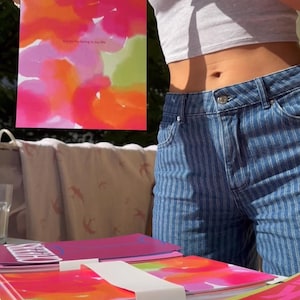 May include: A stack of notebooks and a framed print with colorful abstract art. The print features pink, orange, and green watercolor-style designs with the text "Thanks for being in my life". The notebooks have similar designs.