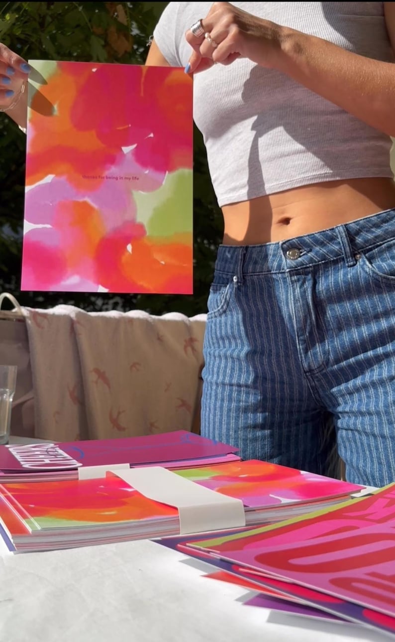 May include: A stack of notebooks and a framed print with colorful abstract art. The print features pink, orange, and green watercolor-style designs with the text "Thanks for being in my life". The notebooks have similar designs.