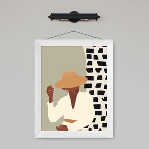 May include: A framed illustration of a person wearing a tan hat and a white shirt, standing in front of a black and white geometric pattern.