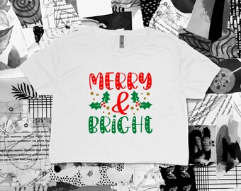 May include: White cropped t-shirt with the text "Merry & Bright" in red, green, and gold lettering. The text is surrounded by small gold dots and green holly leaves with red berries.