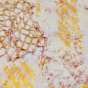 May include: Close-up of a mixed media art piece with gold and white paint and a lace overlay. The background is a light pink with a faint text pattern.