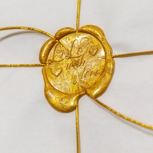 May include: A gold wax seal with the words "Life with Love" and a heart design. The seal is attached to a white surface with gold wire.