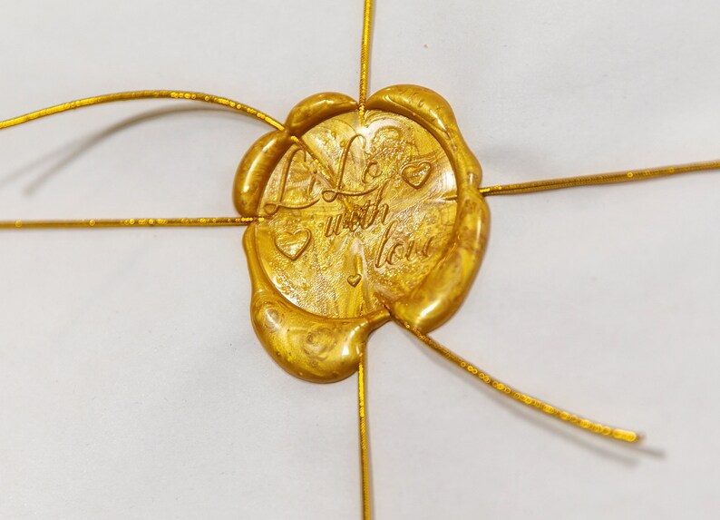 May include: A gold wax seal with the words "Life with Love" and a heart design. The seal is attached to a white surface with gold wire.