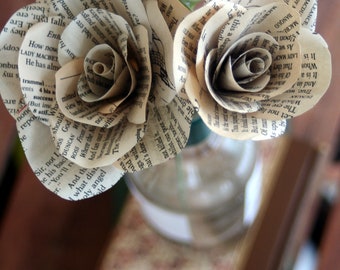 Peut inclure: Trois roses en papier faites à partir de vieilles pages de livres dans un vase en verre transparent. Le vase est posé sur un livre brun.