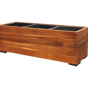 Puede incluir: Una jardinera rectangular de madera con tres compartimentos interiores. La jardinera está construida con madera de color marrón claro y tiene un patrón de vetas natural. Los compartimentos interiores son negros. La jardinera se apoya en pequeños pies negros.