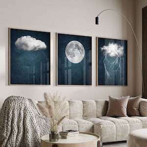 May include: Three framed prints with a blue background and white clouds, moon, and lightning. The prints are hanging on a light beige wall above a white sofa with a throw blanket and cushions.