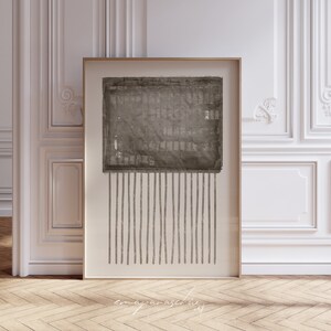 Puede incluir: Una impresión de arte abstracto enmarcada con un esquema de color marrón y blanco. La impresión presenta una forma cuadrada texturizada con líneas verticales que se extienden desde la parte inferior.