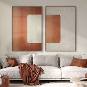 May include: Two rectangular wall art prints in thin wooden frames featuring abstract geometric designs. The left print displays a large terracotta-colored block with vertical lines and a white cutout, while the right print shows a white block with a terracotta-colored cutout.