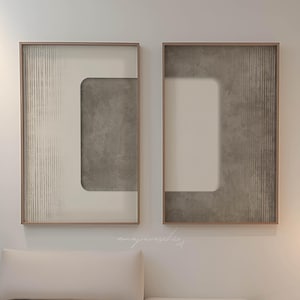 May include: Two framed abstract art prints with a white background and a grey geometric design. The prints are hanging on a white wall above a light beige sofa.