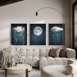 May include: Three framed prints of a moon, a cloud, and a cloud with lightning. The prints are hanging on a white wall above a white couch with pillows.