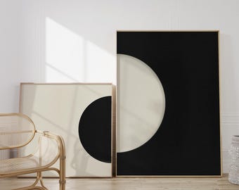 May include: Two framed abstract art prints with black and white geometric shapes. The larger print features a black background with a white crescent shape. The smaller print features a white background with a black circle.