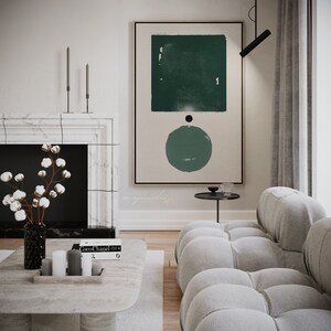 Peut inclure: Un mur blanc avec une peinture abstraite verte et beige, une chemin&eacute;e en marbre blanc, un vase noir avec des fleurs de coton blanches, trois bougies blanches et un canap&eacute; gris avec une table d'appoint noire.