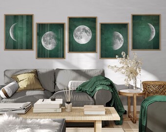 May include: Five framed prints with a green background and white crescent moons in different phases. The prints are hanging on a white wall above a grey sofa with green throw pillows and blankets.