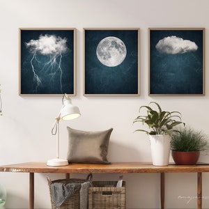 May include: Three framed prints with a dark blue background and white clouds. The left print features a cloud with lightning bolts. The middle print features a full moon. The right print features a cloud.