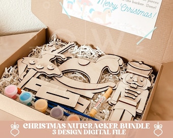 May include: A brown cardboard box with a Nutcracker DIY kit inside. The kit includes wooden pieces of a nutcracker, a rocking horse, and a ballerina. The box also includes paint and glue. The box has a label that says "Nutcracker DIY Kit" and "Merry Christmas!"