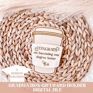 Pode incluir: Porta-cart&atilde;o de presente de madeira em forma de x&iacute;cara de caf&eacute; com o texto "CONGRATS on becoming one degree houer" e um &iacute;cone de chap&eacute;u de formatura. O porta-cart&atilde;o est&aacute; sobre uma superf&iacute;cie tecida. 4 designs inclu&iacute;dos.