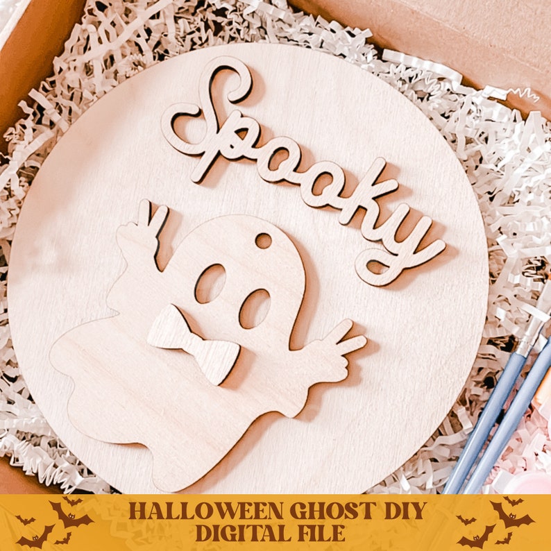 May include: A wooden round sign with the word "Spooky" written in cursive and a ghost with a bow tie. The sign is surrounded by white shredded paper. The text "HALLOWEEN GHOST DIY DIGITAL FILE" is at the bottom of the image.