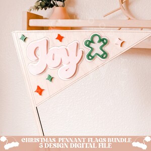 May include: A wooden Christmas pennant flag with the word "Joy" in pink letters and a green gingerbread man. The flag is decorated with red and green stars.