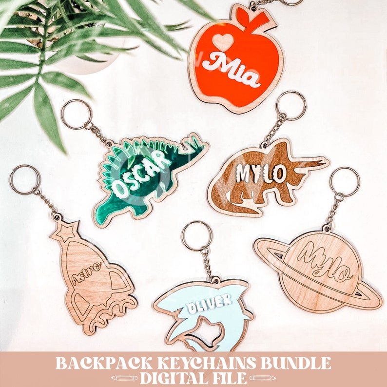 May include: A set of six wooden backpack keychains with different designs and names. The designs include an apple, a dinosaur, a triceratops, a rocket, a shark, and a planet. The names on the keychains are Mia, Oscar, Milo, Astro, Oliver, and Milo.