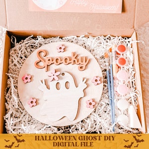 May include: A DIY Halloween ghost craft kit with a wooden circle, paint, brushes, and pink flowers. The circle has the word "Spooky" and a ghost with peace signs.